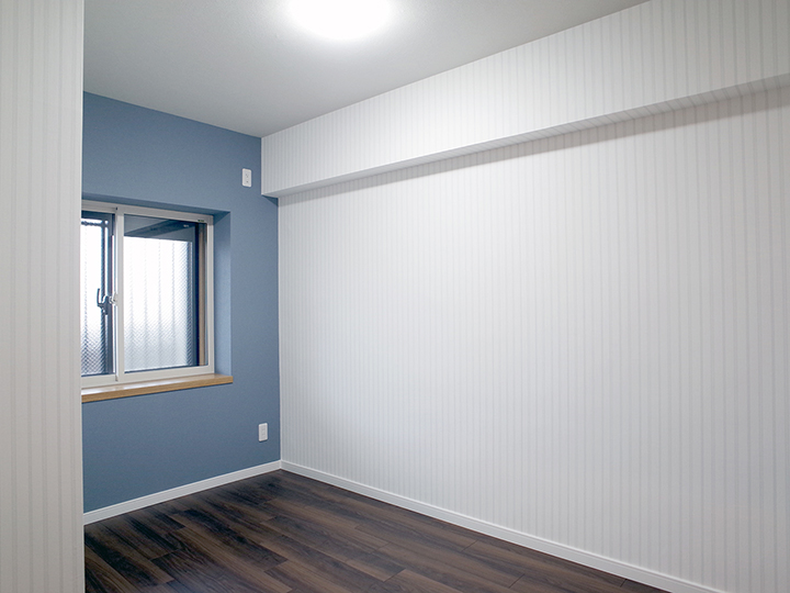 洋室は窓側の壁にアクセントで落ち着いたブルーの壁紙を、全体に淡い色のストライプの壁紙を採用しました。